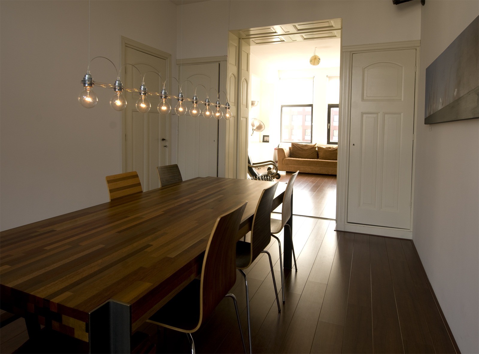 1879 hanglamp met transparante gloeilampen aan een strakke lijn boven een houten eettafel