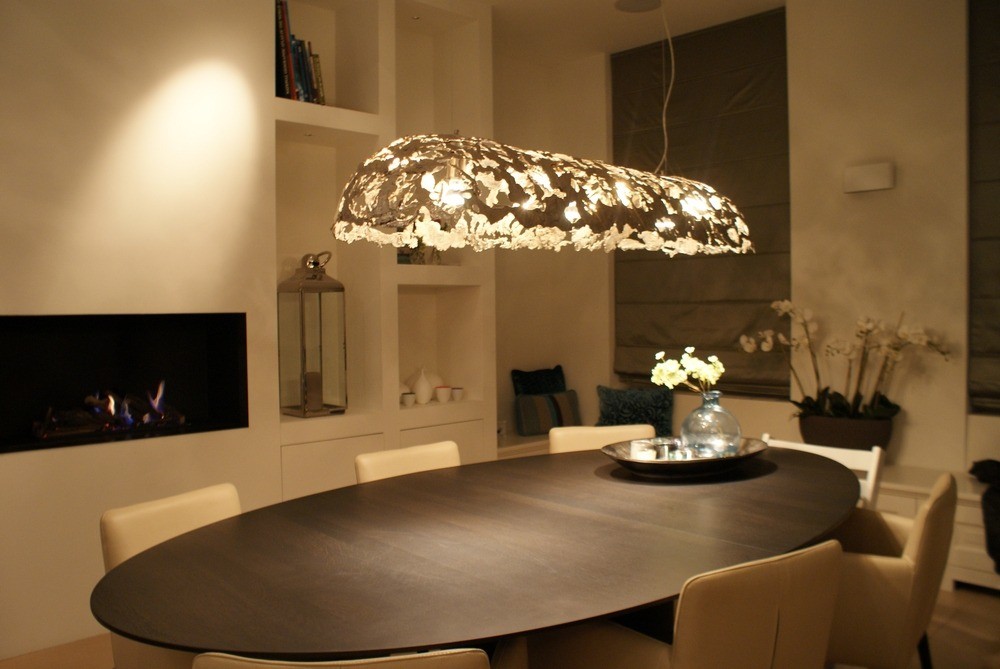 Ovale World of Light pendellamp boven een eettafel bij een open haard